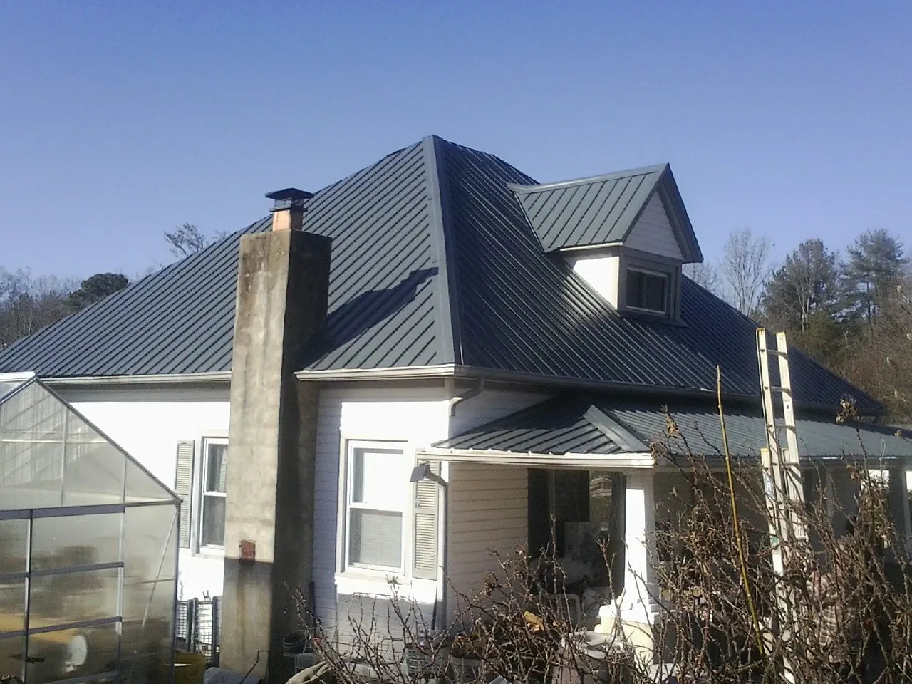 Dark blue standing seam metal roof on a white farmhouse with dormer — Slate & Tile Roof Repair by Roofing Brothers in Custer City
