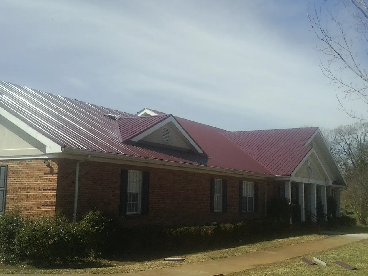 Red metal roof with gabled entries on a long brick building, from a Hail Damage Roof Repair job in Custer City